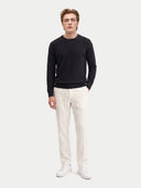 A man modeling a black long-sleeve crewneck sweater, off-white trousers, and white sneakers against a light gray studio background.