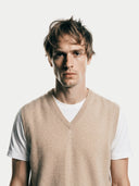 close up front view of a man wearing a beige v-neck sweater vest over a white t-shirt on a plain background #color_beige