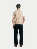 back view of a man wearing a beige vest over a white t-shirt with black pants on a light gray background #color_beige