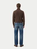 Man wearing a brown sweater and blue jeans on a white background.