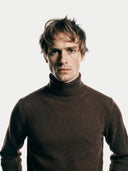 Man wearing a brown turtleneck sweater against a white background.