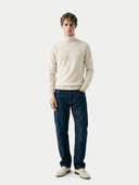 front view of a man wearing a beige turtle neck sweater and blue jeans on a white background #color_off-white
