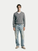 Man wearing a gray sweater and light blue jeans on a white background.