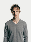 close up front view of a man wearing a gray v-neck sweater.