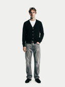 front view of a man wearing a black v-neck cardigan over a white shirt and gray jeans on a white background #color_black
