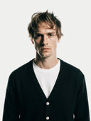 close up of a man wearing a black cardigan over a white shirt on a light gray background #color_black