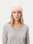 Woman wearing a pink knit beanie with a logo on a white background. #color_pink