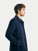 side view of a man wearing a navy blue coat against a white background. #color_navy