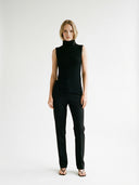 Woman wearing a black sleeveless, turtleneck top and pants on a white background #color_black