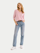 Woman wearing a pink v-neck sweater and light blue jeans on a white background #color_almond-blossom