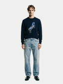 Man wearing a navy sweater with a horse design and light blue jeans on a white background #color_navy