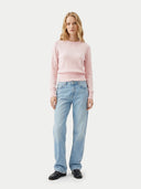 Woman wearing a pink sweater and light blue jeans on a white background #color_peach-blush