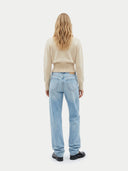 back view of a woman wearing a beige sweater and light blue jeans on a white background #color_beige