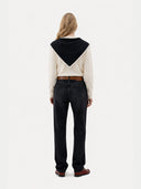 back view of a person wearing a cream sweater with tied a black scarf and dark jeans on a white background #color_black