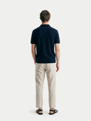 Back view of man wearing a navy polo shirt and beige pants on a white background #color_mood-indigo