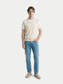 front view of a man wearing a beige v-neck vest, a white t-shirt, blue jeans, and beige loafers on a white background #color-white