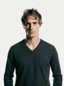 close up front view of a man wearing a dark gray v-neck sweater.