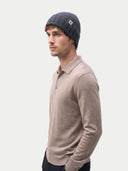 Man wearing a beige long-sleeve shirt and navy knit beanie on a light gray background. #color_charcoal