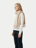 side view of a woman wearing a beige scarf with fringe on a white background. #color_off-white