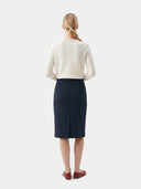 back view of a woman wearing a white sweater and black skirt on a white background. #color_black