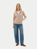 Woman wearing a beige hoodie, white shirt, blue jeans, and brown shoes on a white background. #color_beige