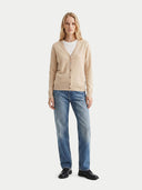 Woman wearing a beige cardigan, white shirt, blue jeans, and black shoes on a white background. #color_beige