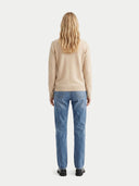 back view of a woman wearing a beige sweater and blue jeans on a white background. #color_beige