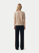 back view of a woman wearing a beige sweater and black pants with a subtle stripe on a white background. #color_beige
