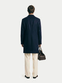 Back view of a man wearing a navy mid-length coat over a white long-sleeve shirt on a white background. #color_navy