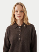 A blonde woman wearing a dark brown long-sleeve knit polo shirt with a buttoned collar, photographed against a clean light gray studio background.