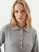 A close-up of a blonde woman wearing a light gray ribbed knit polo shirt with a buttoned collar and three buttons.