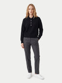 A woman modeling a black long-sleeve polo-knit sweater, dark gray trousers, and white sneakers against a light gray studio background.
