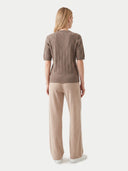 A woman shown from the back wearing a taupe brown short-sleeve cable-knit sweater and beige wide-leg trousers against a light gray studio background.