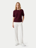 front view of a woman wearing a wine red color short sleeves cashmere top and white pants.