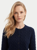A blonde woman wearing a navy blue cable-knit button-front cardigan sweater, photographed against a clean light gray studio background.