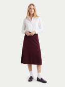 A woman modeling a white long-sleeve button-up shirt and a dark burgundy midi skirt, paired with white socks and dark loafers, against a light gray studio background.