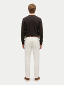 A man viewed from the back wearing a dark brown long-sleeve knit sweater, off-white trousers, a brown belt, and brown slip-on shoes, against a light gray studio background.