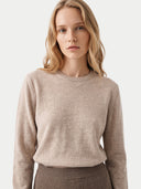 A woman wearing a light beige crewneck knit sweater and a brown ribbed skirt, photographed against a clean off-white studio background.