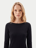 A blonde woman wearing a black long-sleeve boat-neck top, photographed against a clean light gray studio background.