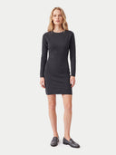 A woman modeling a dark charcoal gray long-sleeve knit mini dress with black leather loafers, standing against a light gray studio background.