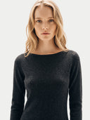 A blonde woman wearing a dark charcoal gray long-sleeve knit sweater with a boat neckline, photographed against a clean light gray studio background.