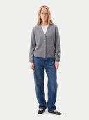A woman stands against a light gray studio background wearing a heather gray button-front cardigan over a white top, blue jeans, and black flats.