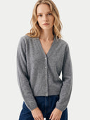 A woman wearing a gray button-front cardigan sweater and dark blue jeans, photographed against a clean light gray studio background.