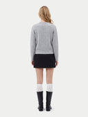 A model shown from the back wearing a light gray ribbed knit sweater, a black mini skirt, white socks, and black knee-high boots against a plain light gray background.