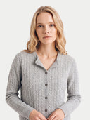 A woman with blonde hair wearing a light gray cable-knit button-up cardigan sweater, photographed against a solid light gray background.