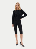 A woman modeling a black textured knit cardigan with buttons, paired with black cropped capri pants and black pointed-toe heels, against a light gray studio background.