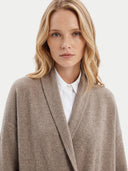 A blonde woman wearing a light brown shawl collar cardigan over a white collared shirt, photographed against a clean off-white background.