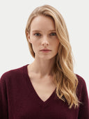 A blonde woman wearing a burgundy V-neck knit sweater, photographed against a clean light gray studio background.
