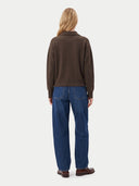 A woman viewed from behind wearing a dark brown long-sleeve knit top, blue jeans, and brown leather shoes against a light gray studio background.