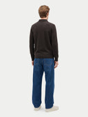 A man viewed from the back wearing a dark brown long-sleeve knit polo sweater, blue jeans, and off-white sneakers, standing against a light gray studio background.
